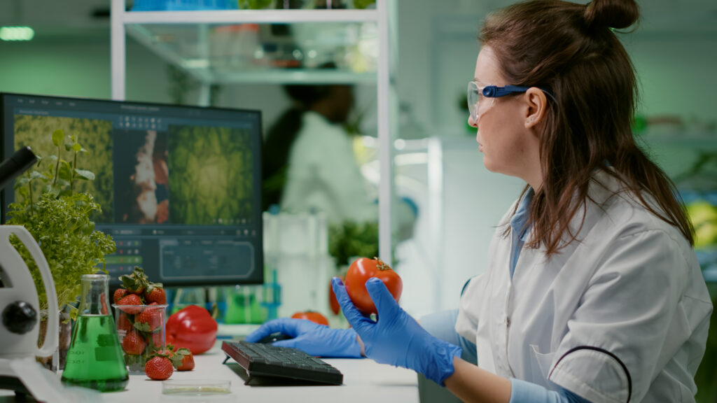 Farmacéutica inspeccionando un tomate en un laboratorio para garantizar la seguridad alimentaria.